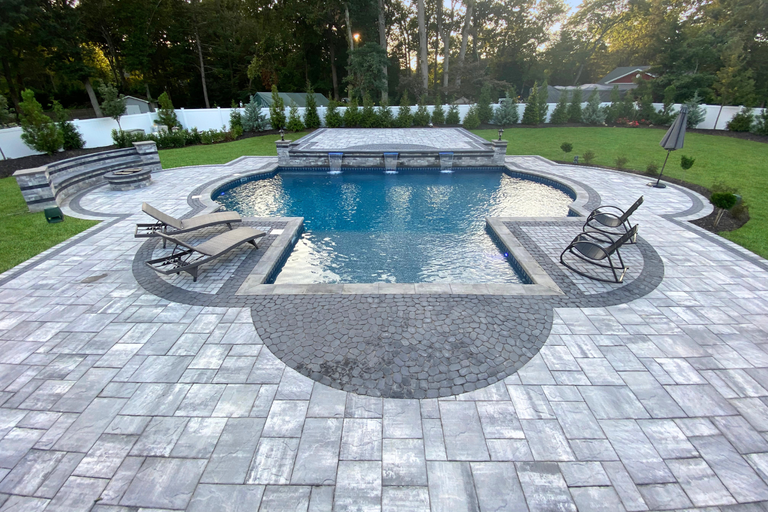 Inground pool with stone paver patio, lounge chairs, and white privacy fence in Fort Salonga NY — Flawless Masonry