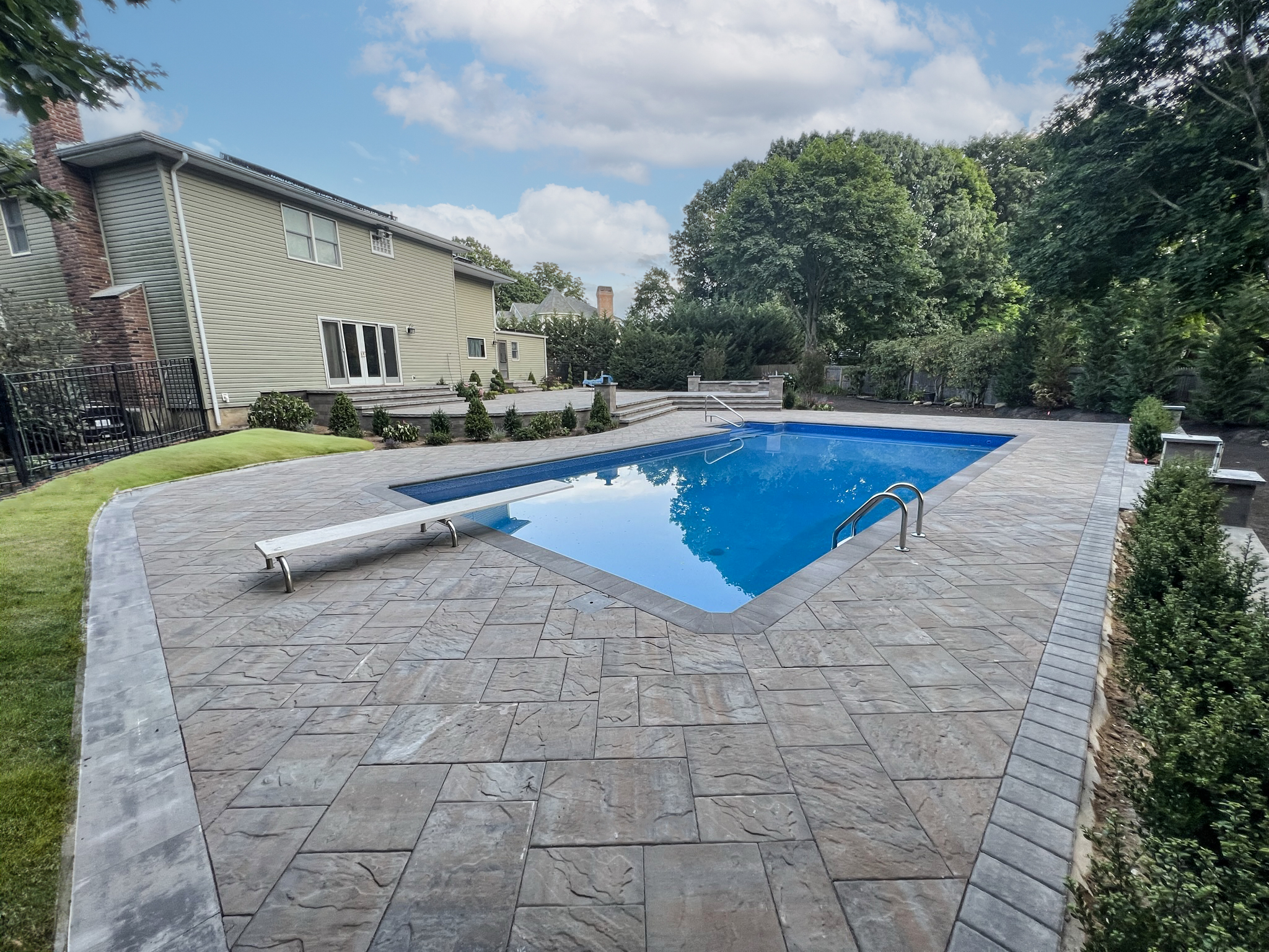 Stamped paver pool deck in textured slate pattern wrapping rectangular inground pool on Long Island colonial home — Nassau County patio installation
