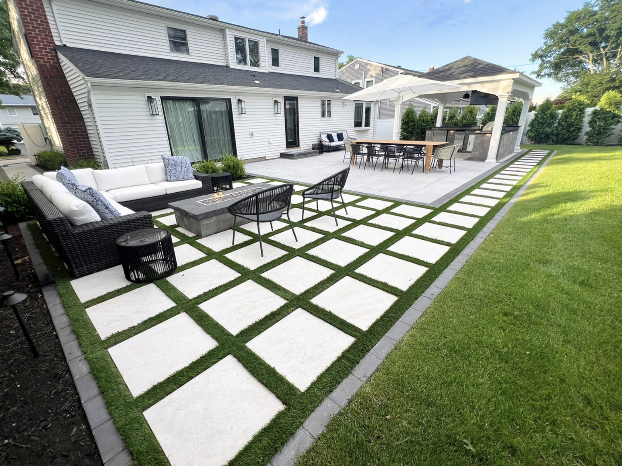 Modern large-format paver patio with synthetic turf grid pattern, fire table lounge, and pergola outdoor kitchen — Long Island patio builder