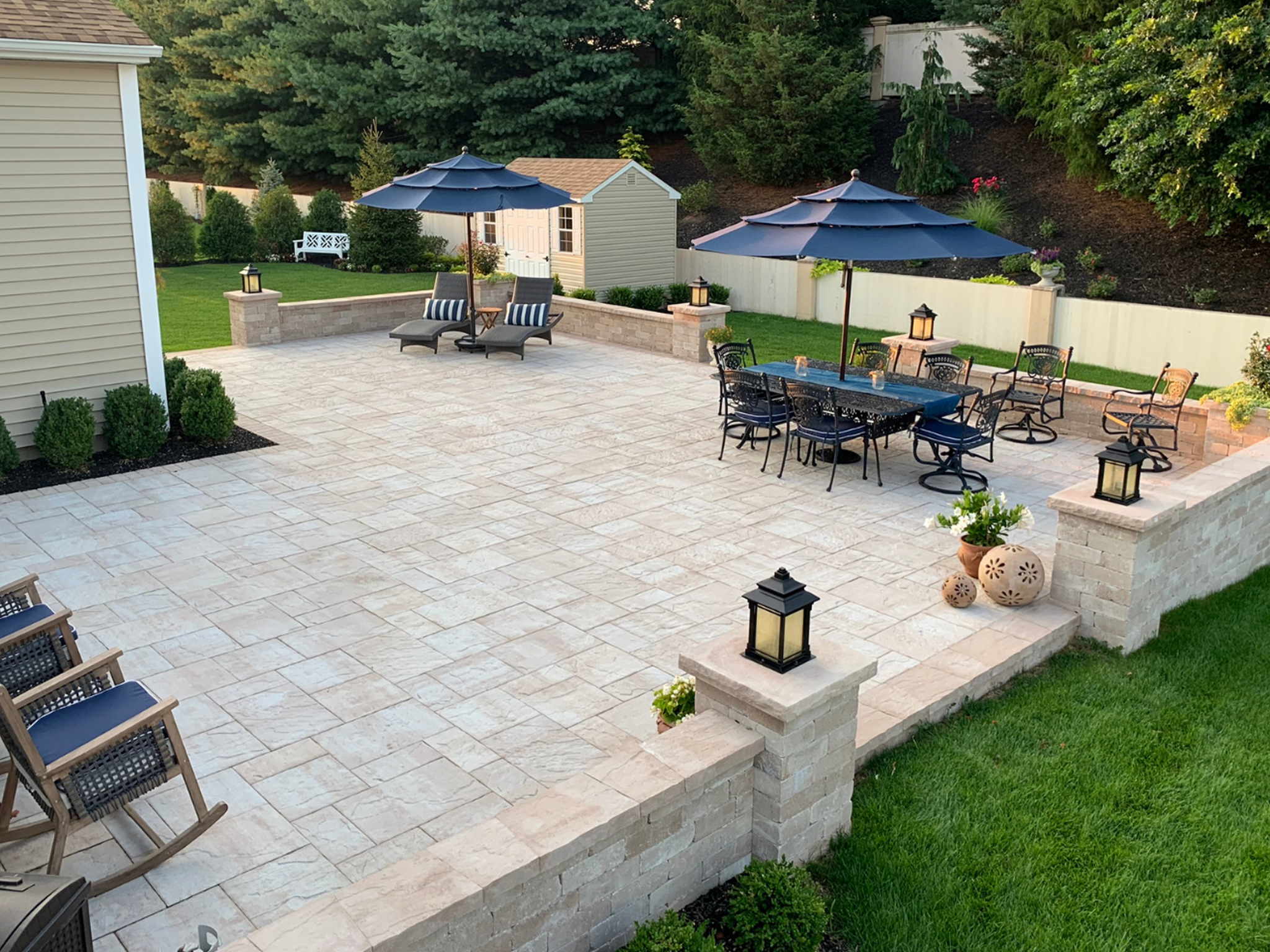 Raised Cambridge paver patio with full-perimeter block retaining wall, outdoor dining set, and landscape lighting — Long Island NY