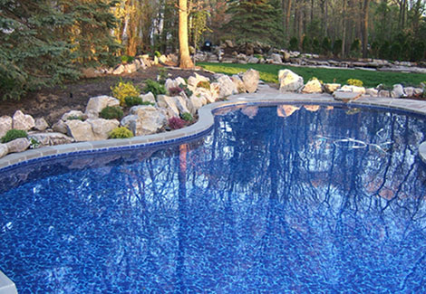 Kidney shaped in ground pool with stone work and tree beds