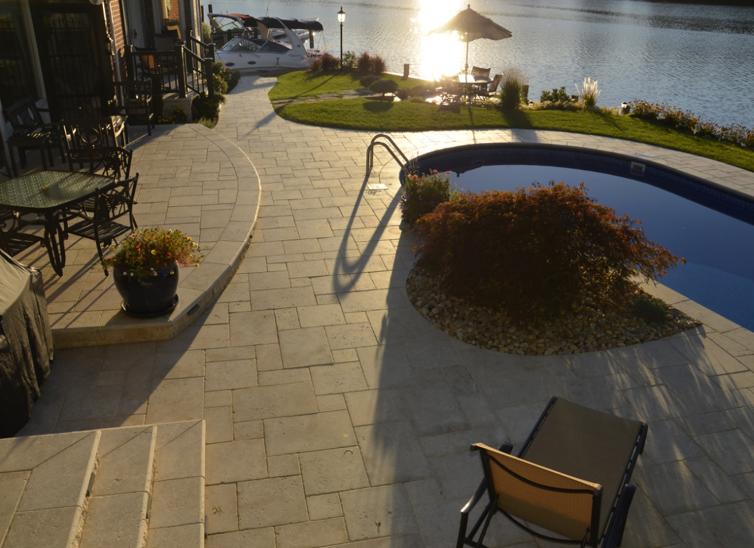 Pool on a property that sits on the shoreline with retaining wall and masonry patio