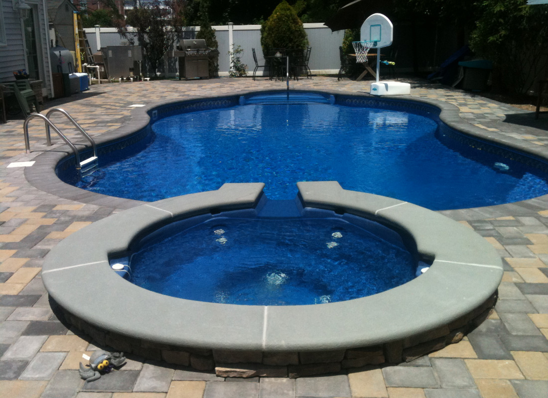 In-ground pool with attached hot tub. Hot tub has water feature spilling into the pool