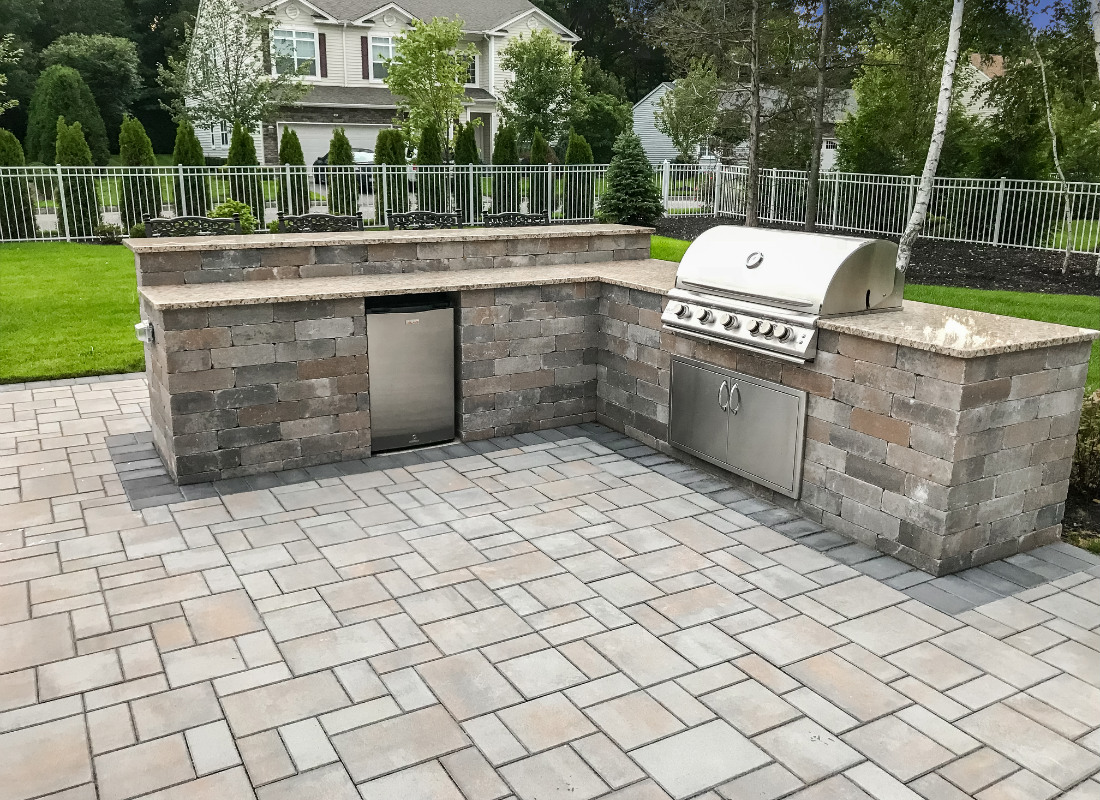 L-shaped stone outdoor kitchen with fridge and grill