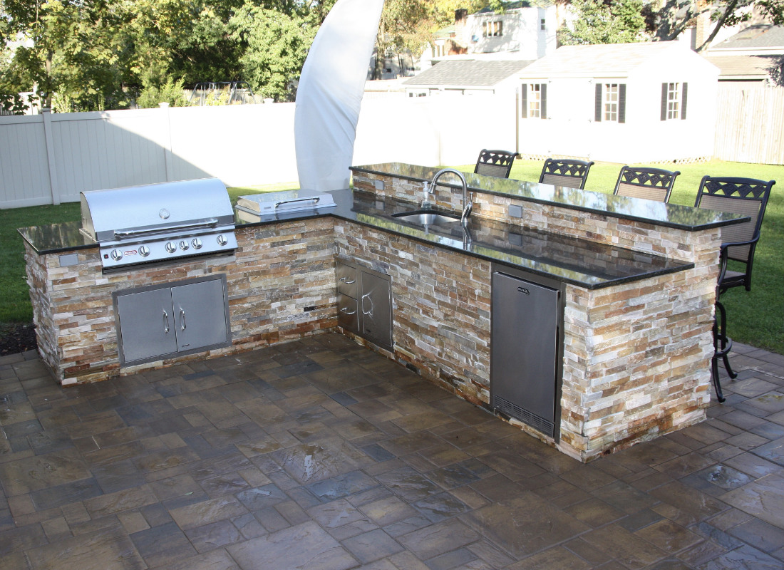 Large L-shaped outdoor kitchen with BBQ, stove top, sink, storage drawers, and refrigerator