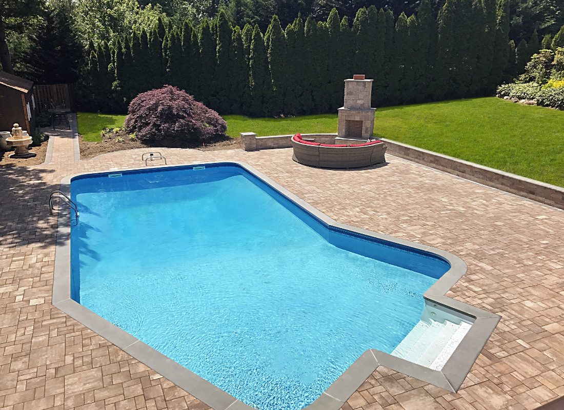 In-ground pool with patio built around it and custom fire pit installed in the far corner