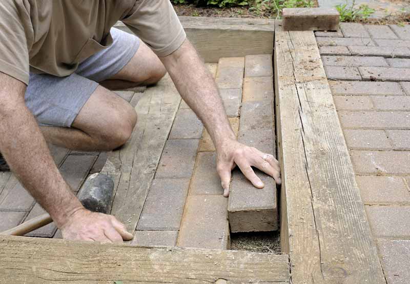 A man is laying bricks to build a pathway, aligning each brick carefully by hand.