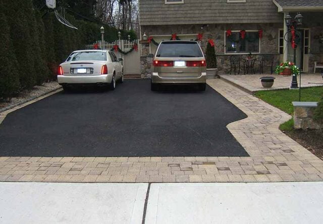 Two cars parked on a newly paved driveway with decorative brick edging and holiday decorations on a house's facade.