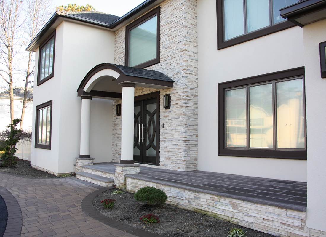 Modern two-story house with stone and stucco exterior, arched doorway, and large windows, in daylight.