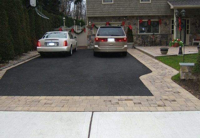 A paved driveway with two parked cars in front of a house decorated with red bows and wreaths. The driveway features a stone pathway that beautifully separates the cars, leading to the entrance.