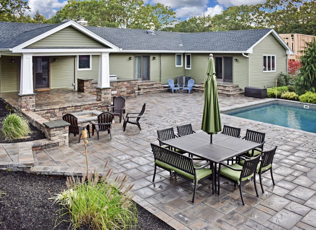 A spacious backyard featuring a swimming pool, a dining table with chairs, and a house with large windows and a patio area.