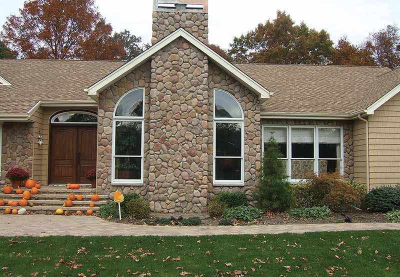 A suburban house with a stone facade, wooden front door, and a lawn decorated with pumpkins.