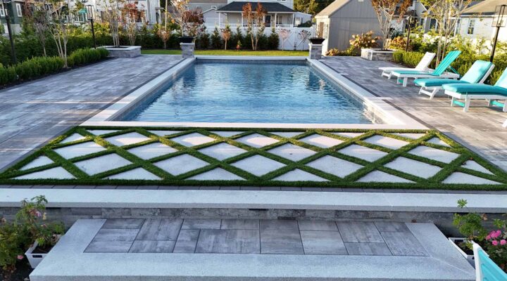 Backyard with rectangular swimming pool, surrounded by stone tiles and greenery. Four turquoise lounge chairs are placed beside the pool.